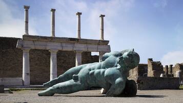 A classical statue of a reclining figure in an outdoor setting with ancient columns and ruins in the background.