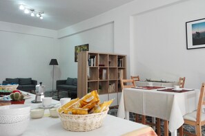 A dining area with a table set for two, a bookshelf, and a sofa in the background. - B&B La Primula (Pompei)
