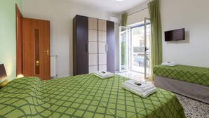 Habitación de hotel con dos camas, un armario, un televisor y una puerta de vidrio corrediza al exterior.