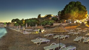 Une plage avec des transats et des parasols, une mer calme et des bâtiments en arrière-plan.