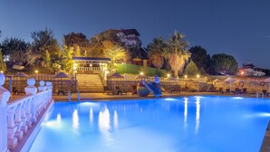 Une piscine avec une terrasse en pierre et un kiosque en arrière-plan.
