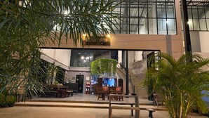 Un espacio interior amplio con techos altos, que incluye una zona de estar con muebles de madera y plantas en macetas.