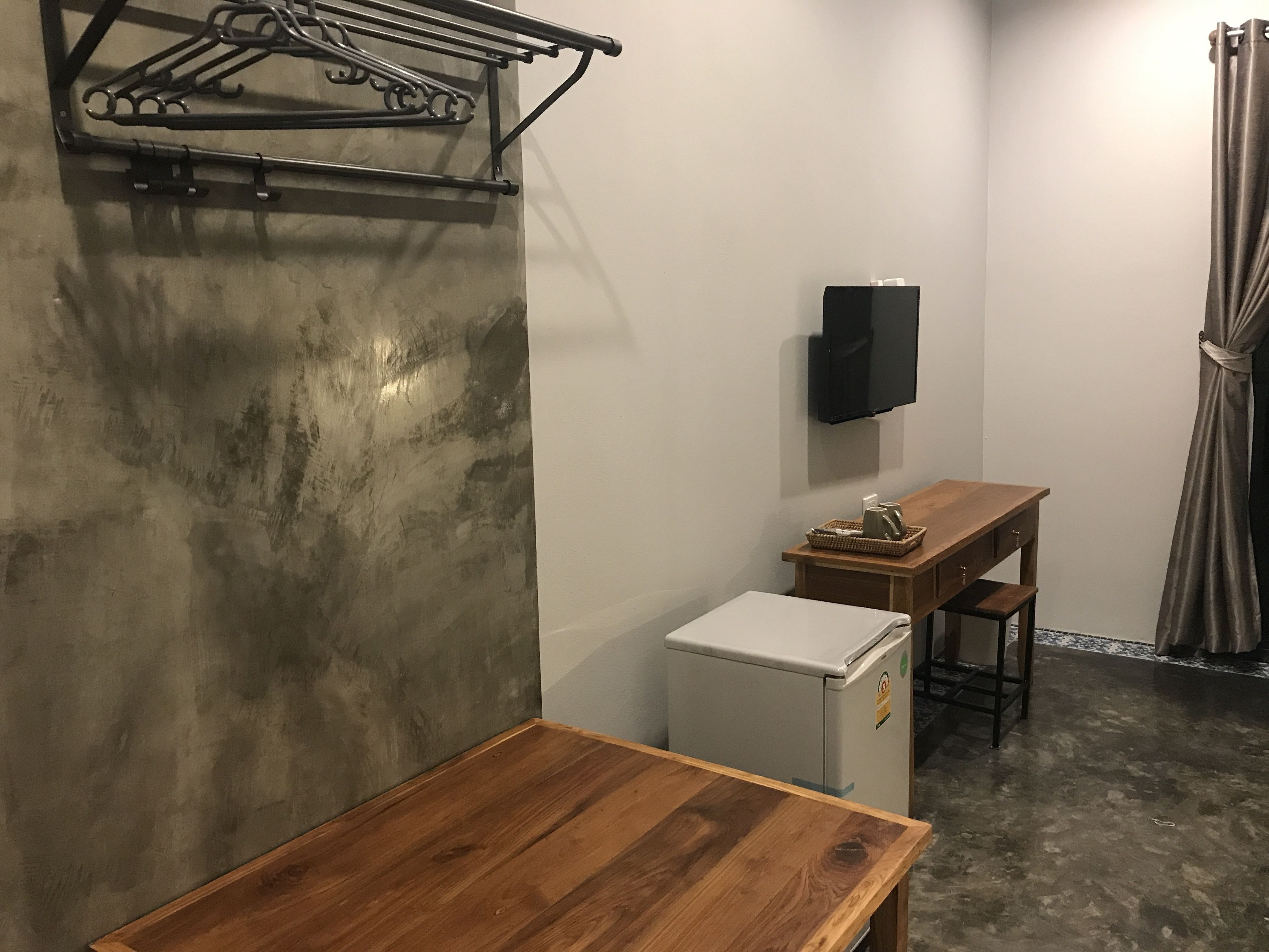 A compact room with a wooden table, a small refrigerator, a wall-mounted TV, and a towel rack.