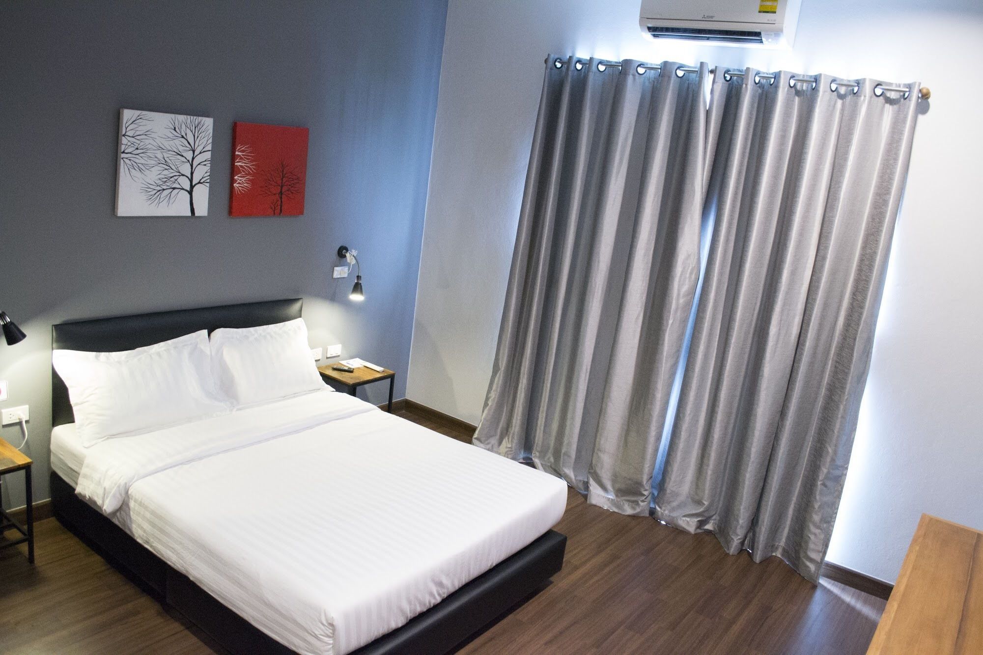 A neatly made bed in a hotel room with a headboard, a bedside table with a lamp, and a curtain.