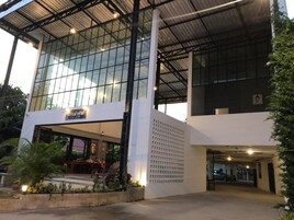 A modern building with a glass facade, a covered entrance, and a parking area.