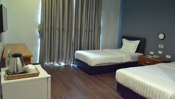 Quarto de hotel com duas camas, uma mesa pequena com chaleira, mesa de cabeceira com telefone e relógio na parede.