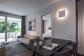 Habitación de hotel moderna con sofá, mesa de comedor y ventana grande con vistas a la vegetación.