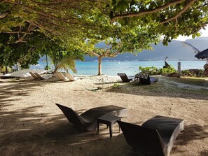 Un salon de plage doté de meubles en osier, d’une table et offrant une vue sur la mer et les montagnes.