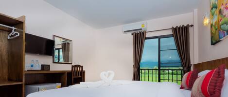 A hotel room with a large bed, a TV, a desk with a mirror, and a view of the outdoors.