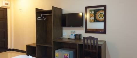 A hotel room with a bed, a desk with a chair, a television, a small refrigerator, and a wardrobe.