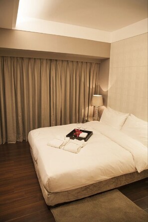 Habitación de hotel con una cama bien hecha, una mesita de noche con lámpara y una bandeja con una flor y vasos.
