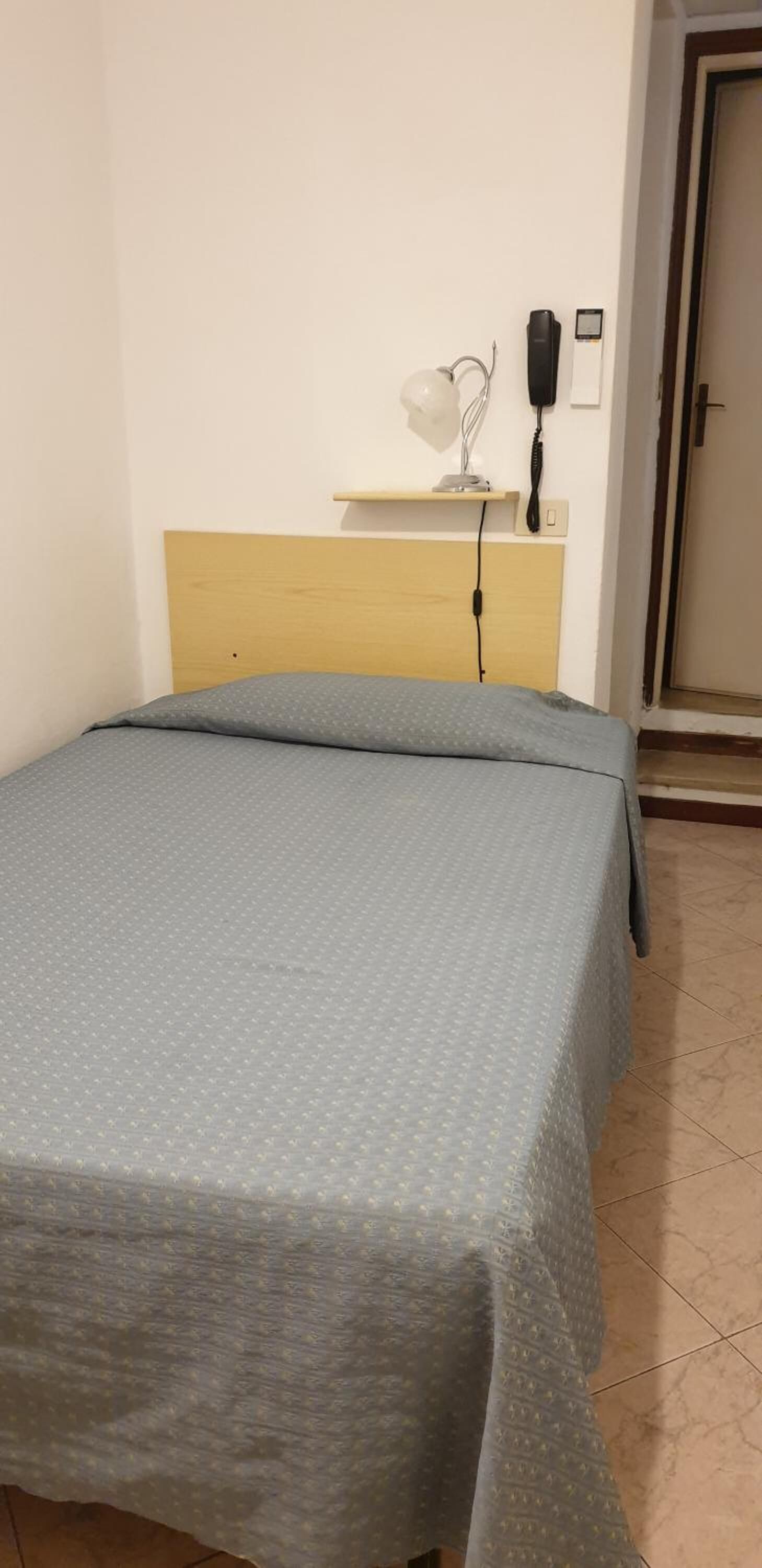 Uma cama de solteiro com cabeceira de madeira, mesa de cabeceira com abajur e telefone na parede.