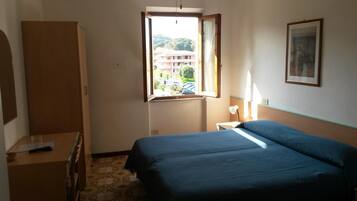 Un dormitorio con cama, escritorio, armario, ventana y un cuadro en la pared.