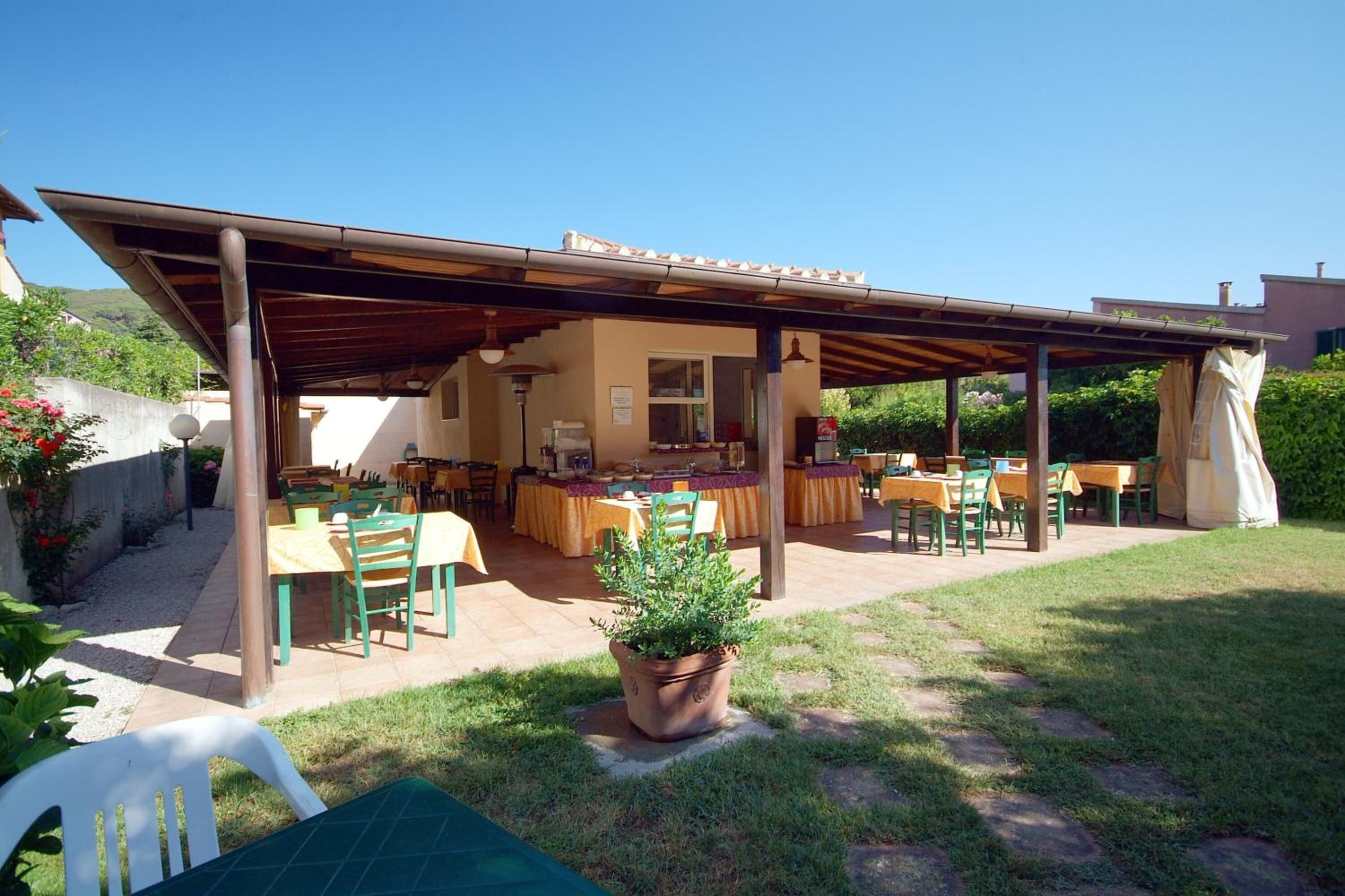 An outdoor patio with multiple tables and chairs, a pergola, and a potted plant.
