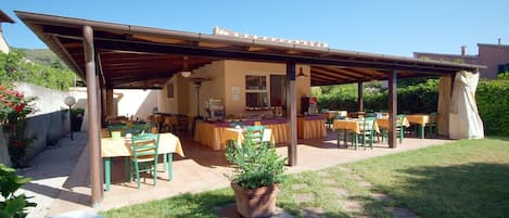 Un patio al aire libre con varias mesas y sillas, una pérgola y una planta en maceta.
