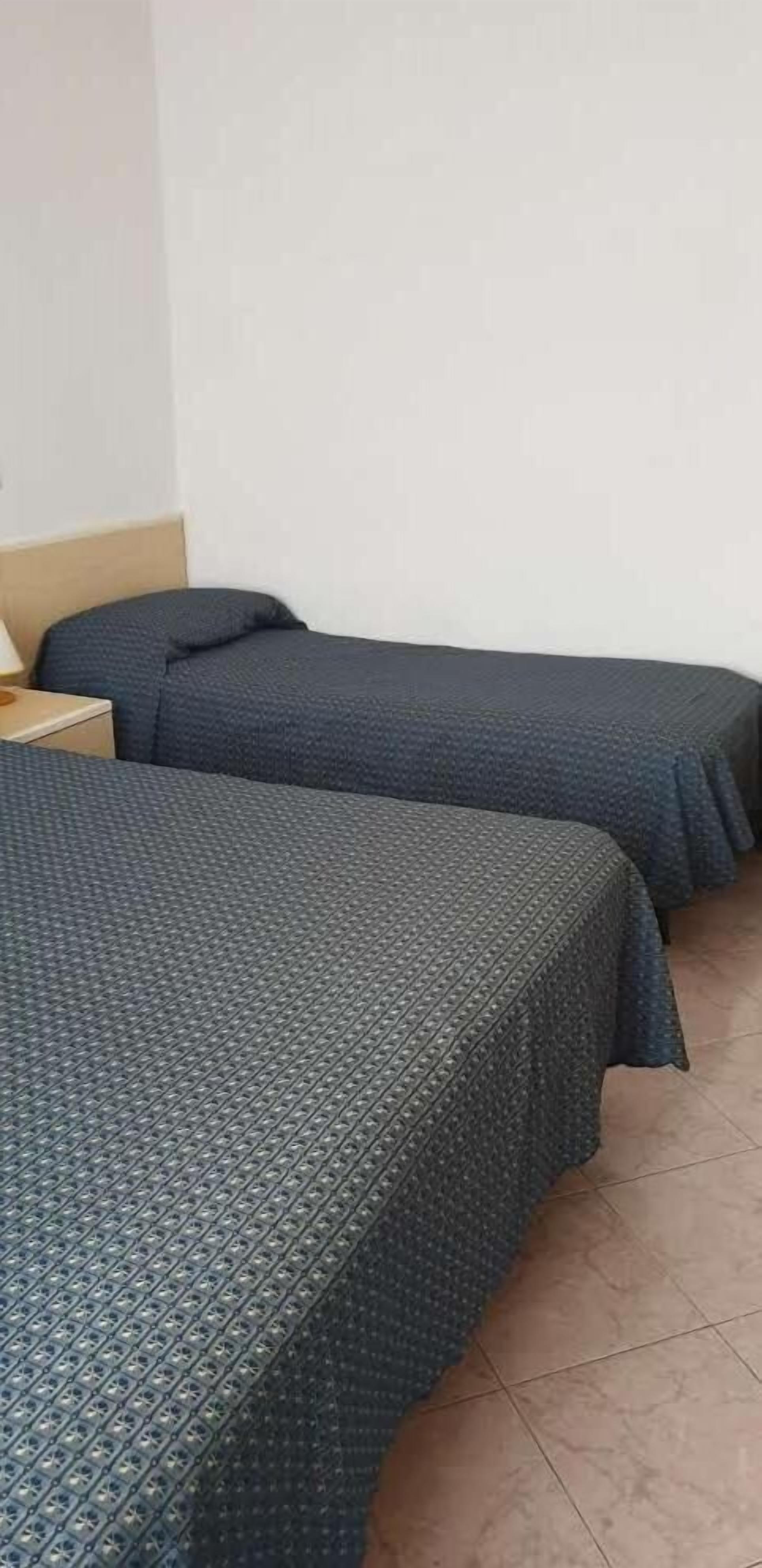 Une chambre avec deux lits, chacun recouvert d’une couvre-lit à motifs, et comprenant une table de chevet et une lampe.