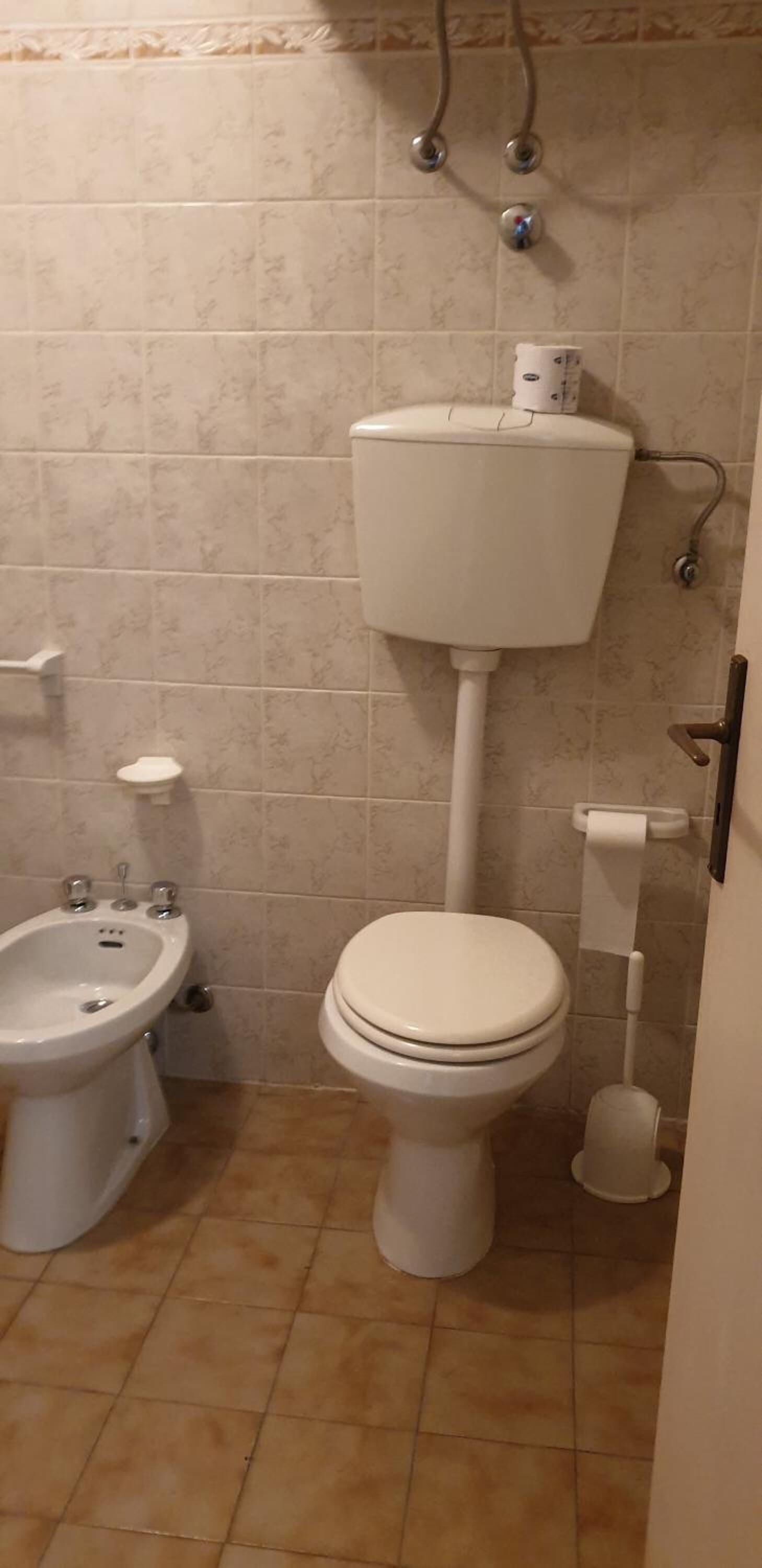 A small bathroom with a toilet, bidet, and a toilet paper holder.
