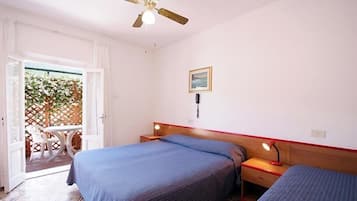 Une chambre avec deux lits, un ventilateur de plafond, une table de chevet avec une lampe et une fenêtre donnant sur un paysage verdoyant.