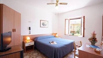 Ein Schlafzimmer mit einem Bett, einem Schreibtisch, einem Fernseher, einem Deckenventilator, einem Fenster und einem an der Wand befestigten Telefon.