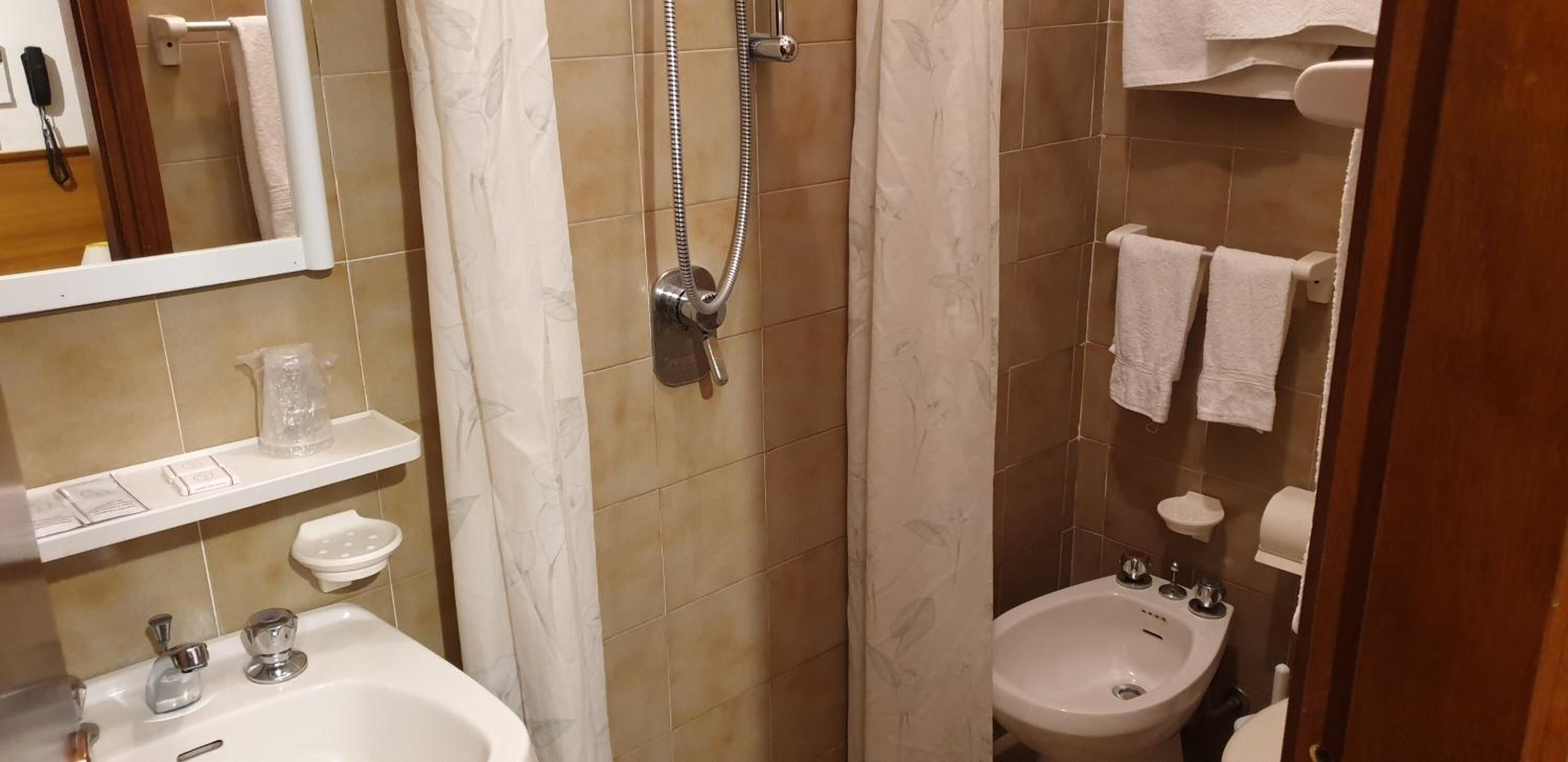 A bathroom with a shower, sink, and bidet. There are towels and toiletries on the shelves.