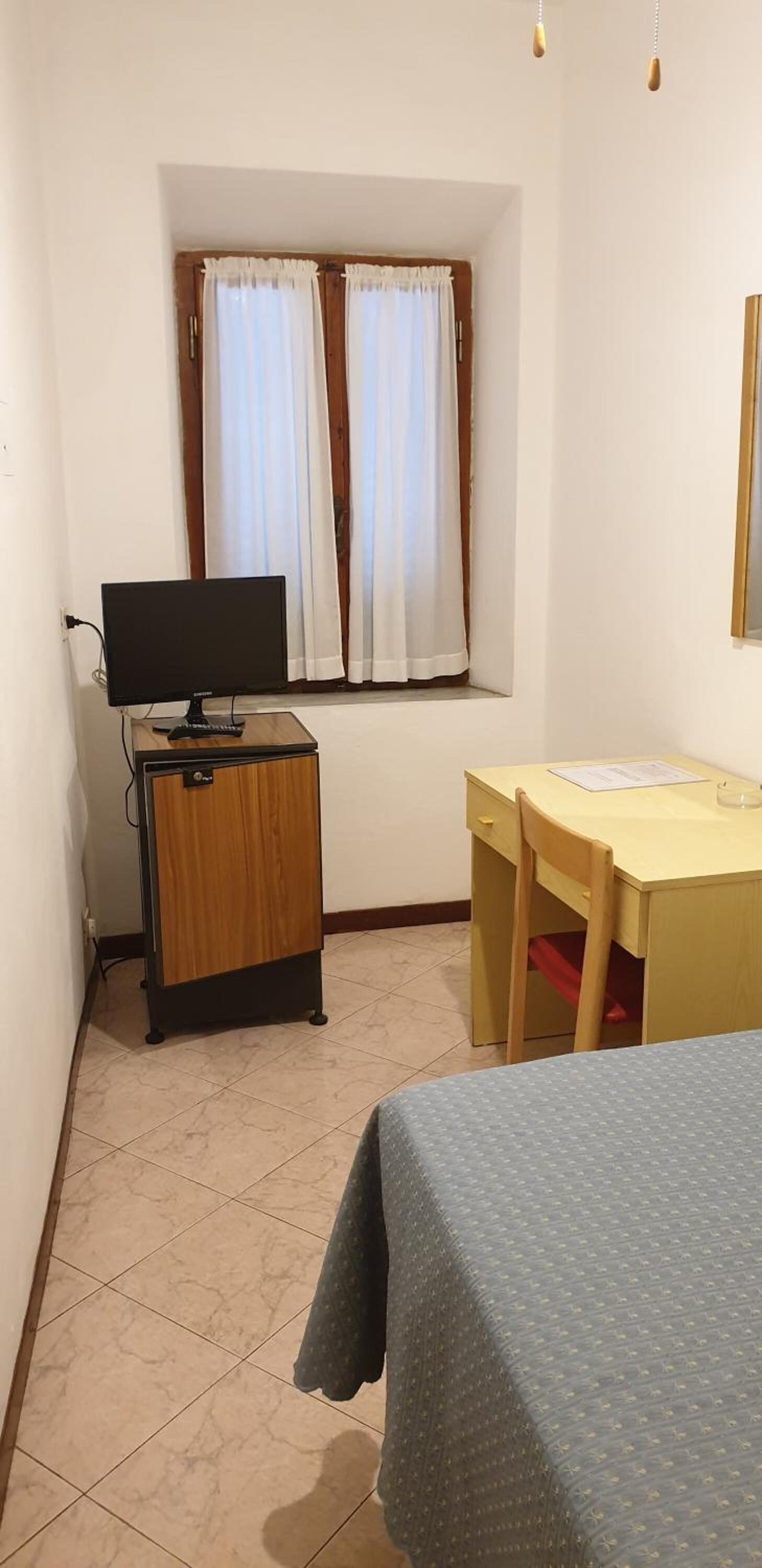 A small room with a bed, a desk, a chair, a television, and a window with curtains.