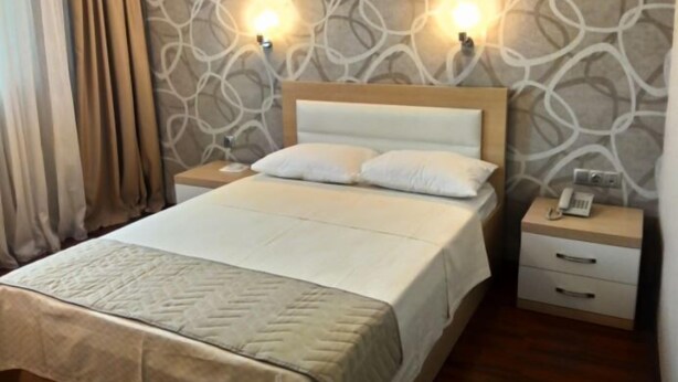 A hotel room with a bed, two bedside tables, a nightstand, and a wall with a patterned design.