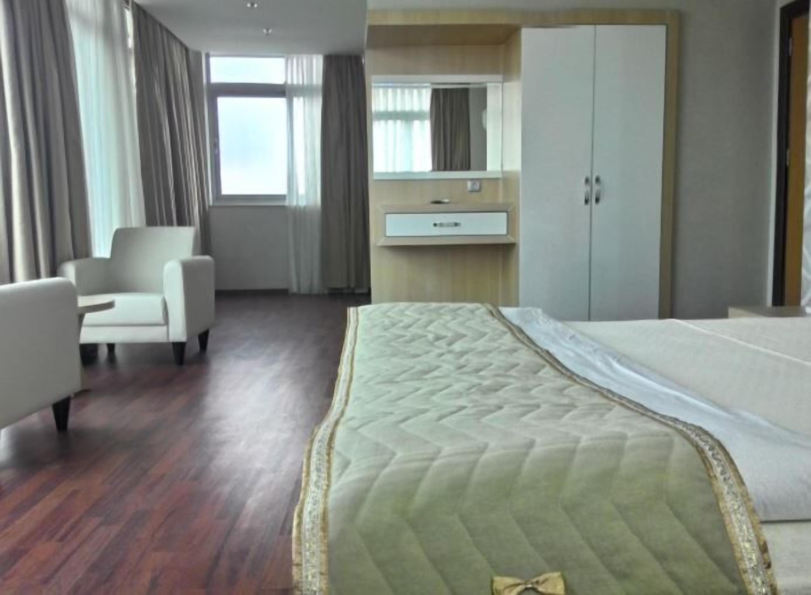 A hotel room with a bed, a chair, a desk, and a wardrobe.