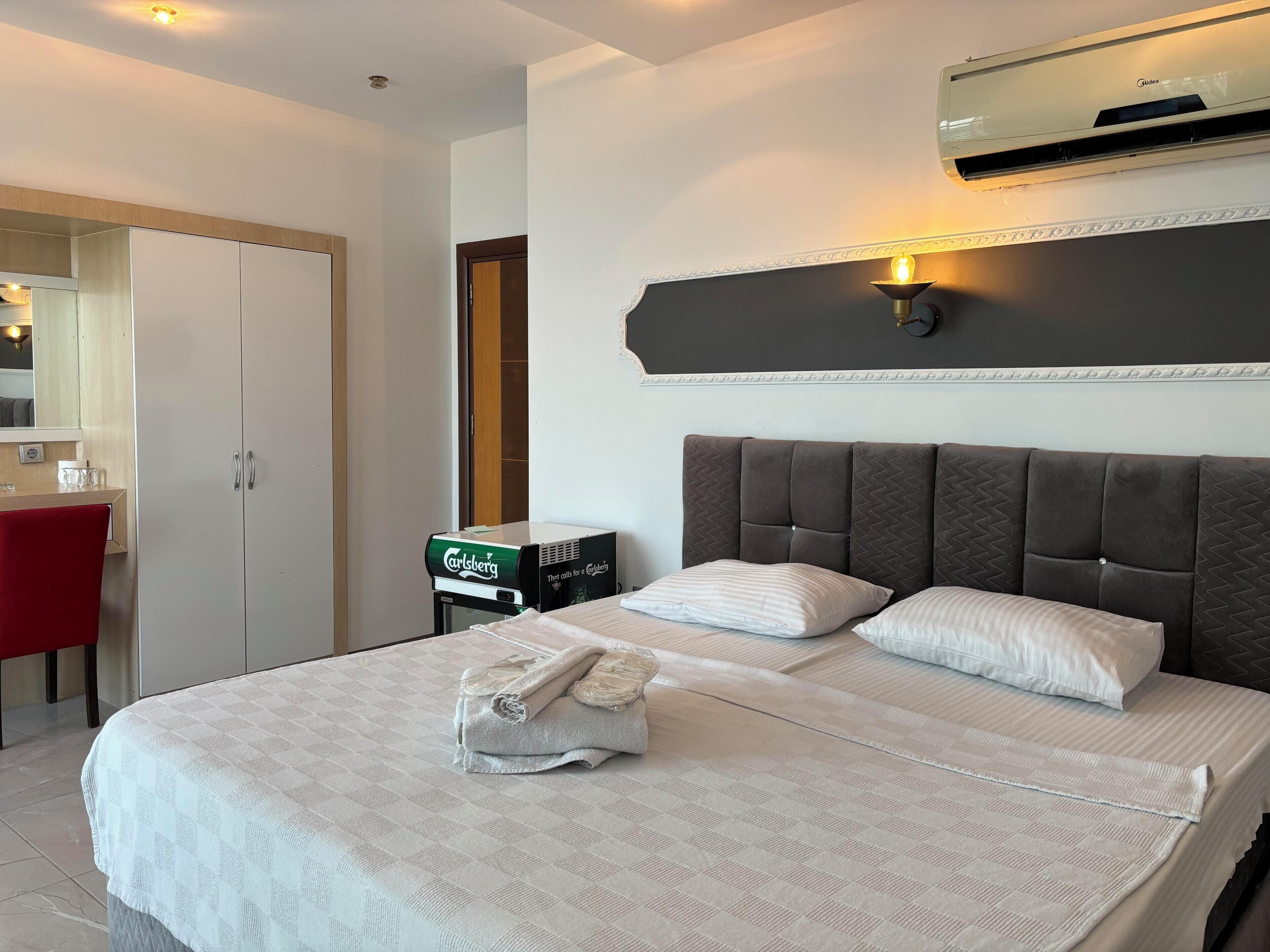 A hotel room with a large bed, a minibar, a desk with a chair, and a wardrobe.