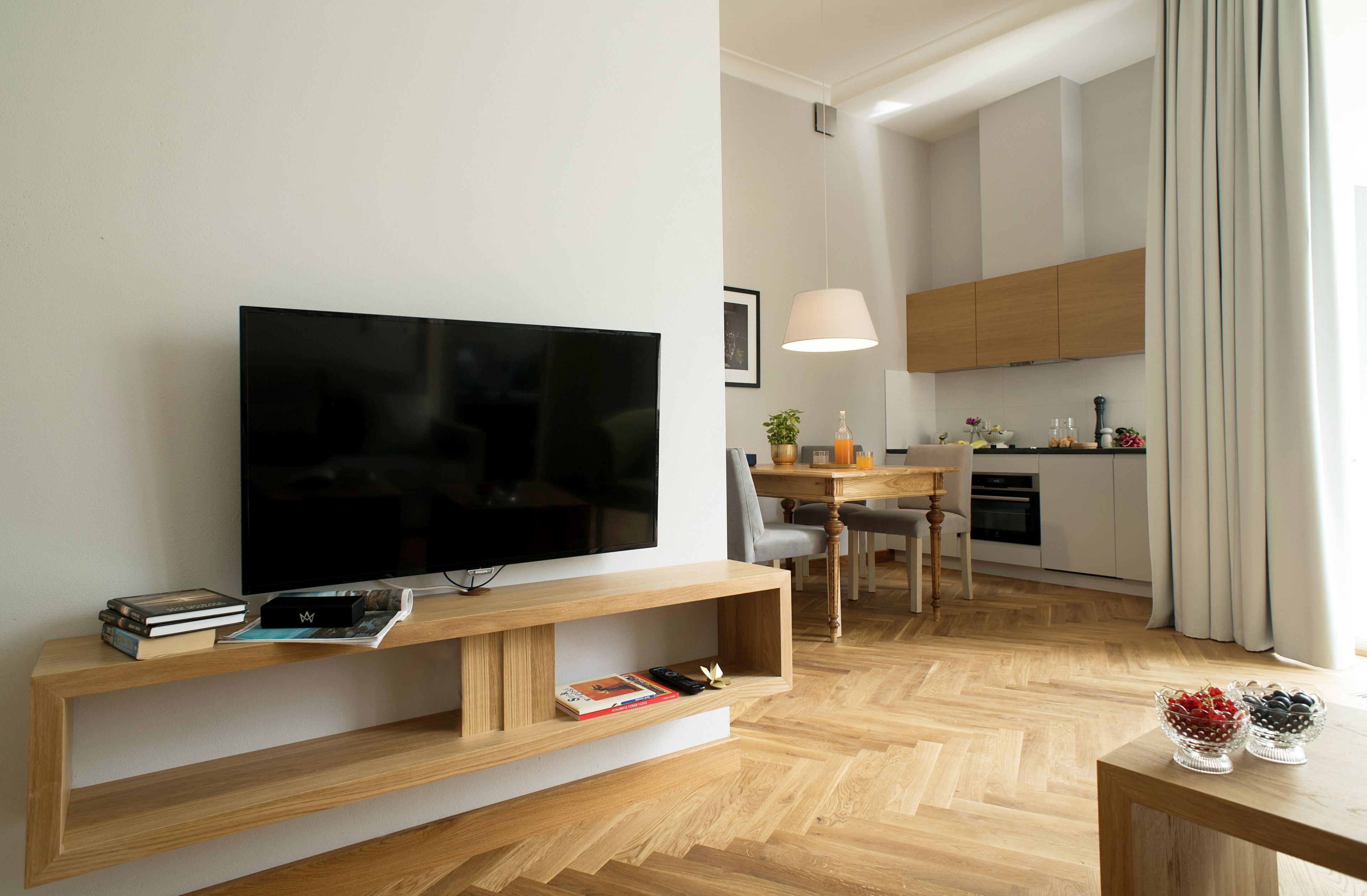 A modern living room with a flat-screen TV, wooden entertainment unit, and a dining area with a table and chairs.