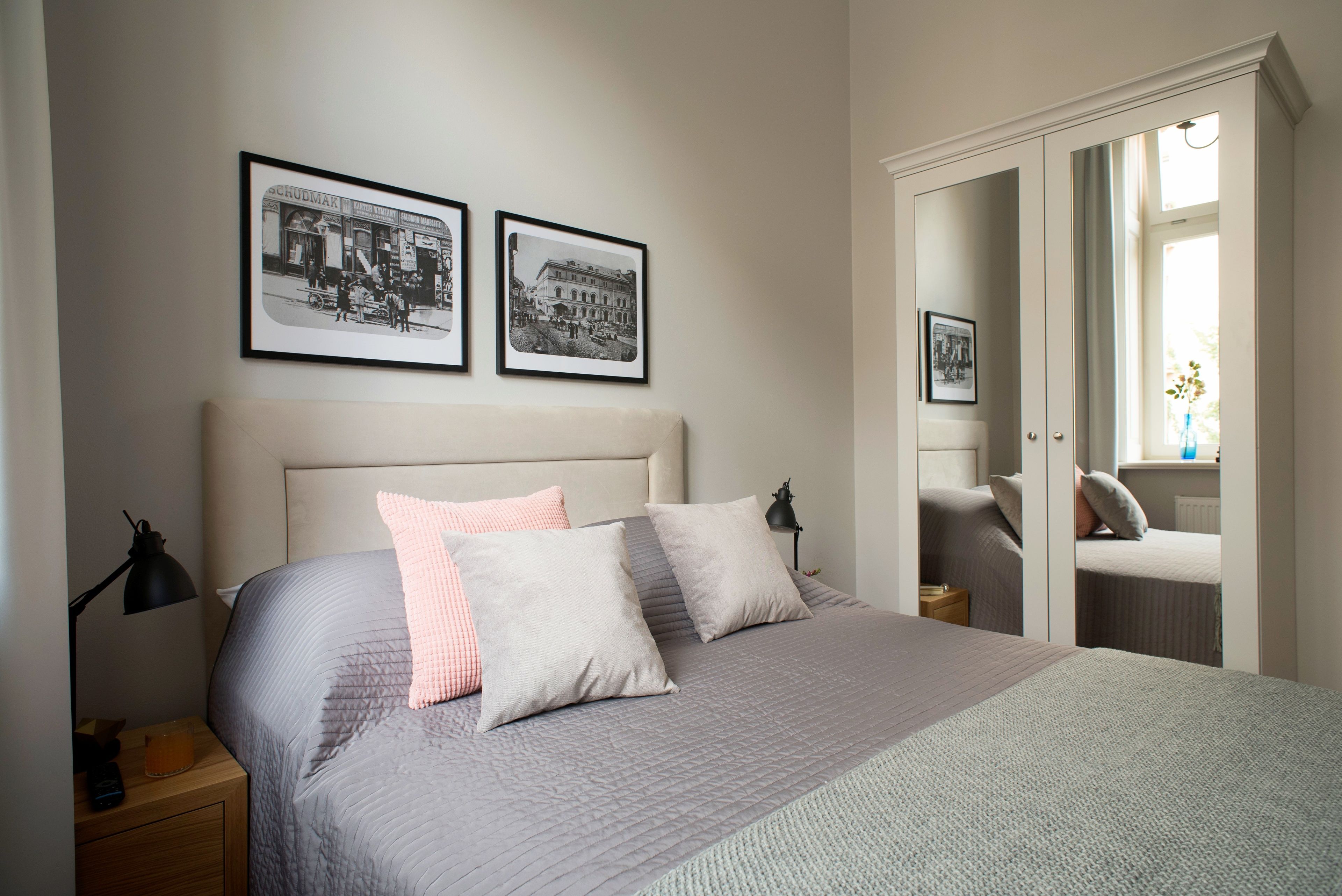 Une chambre à coucher avec un lit, deux tableaux encadrés accrochés au mur, une table de chevet et un miroir dans la pièce adjacente.