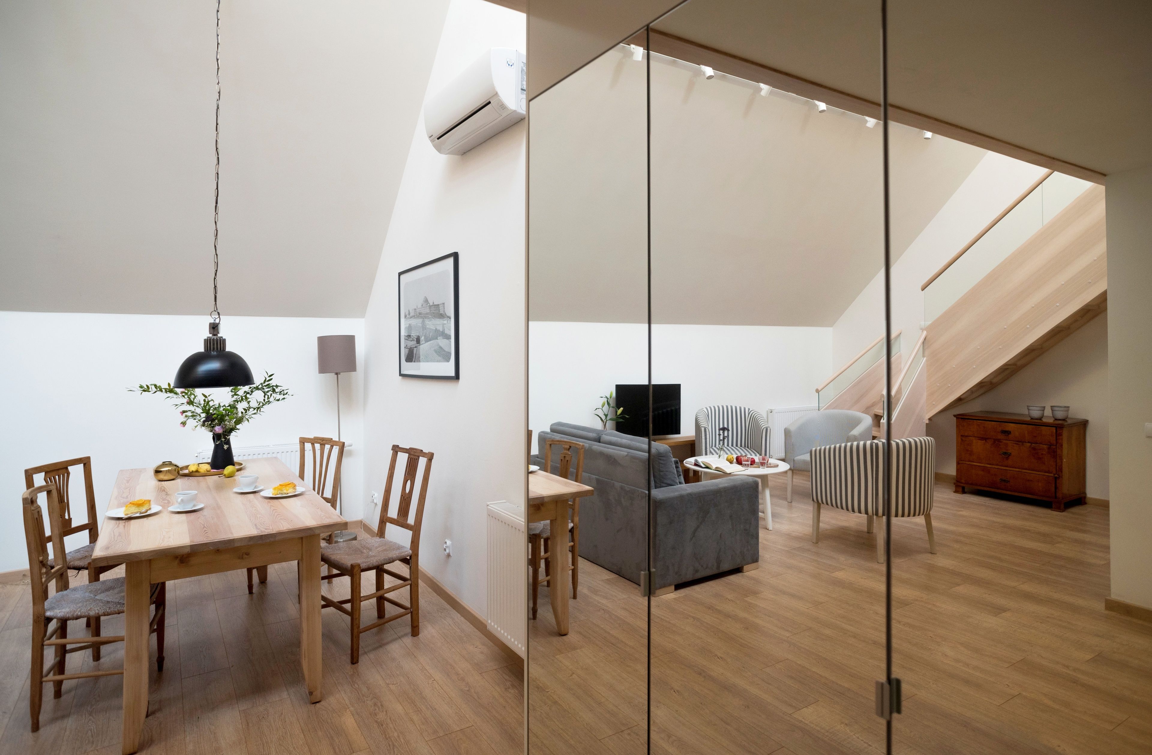Un appartement moderne de style « loft », comprenant un coin repas, un canapé gris, un téléviseur et un escalier.