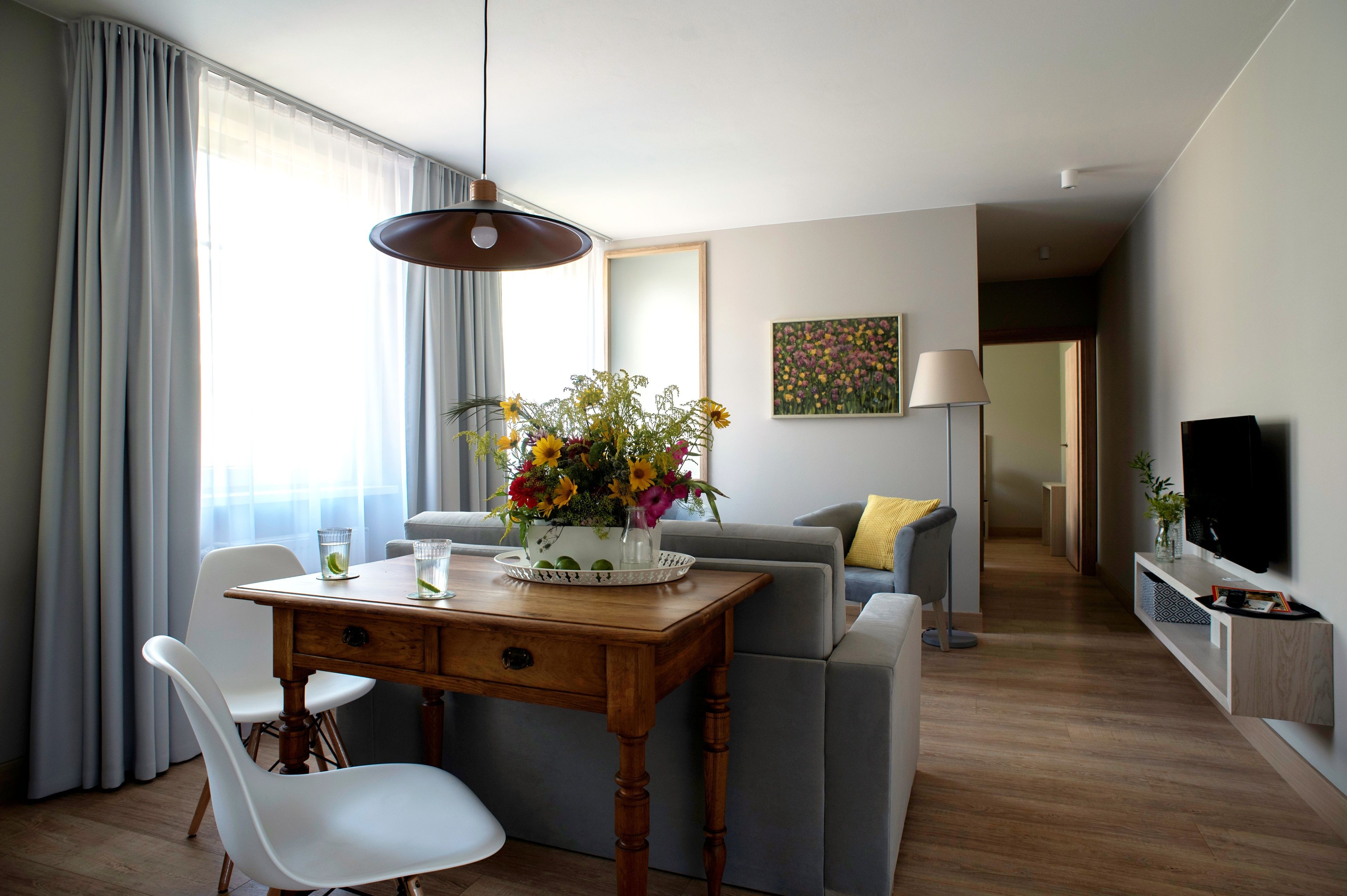 A modern living room with a dining area, a sofa, a TV, and a painting on the wall.
