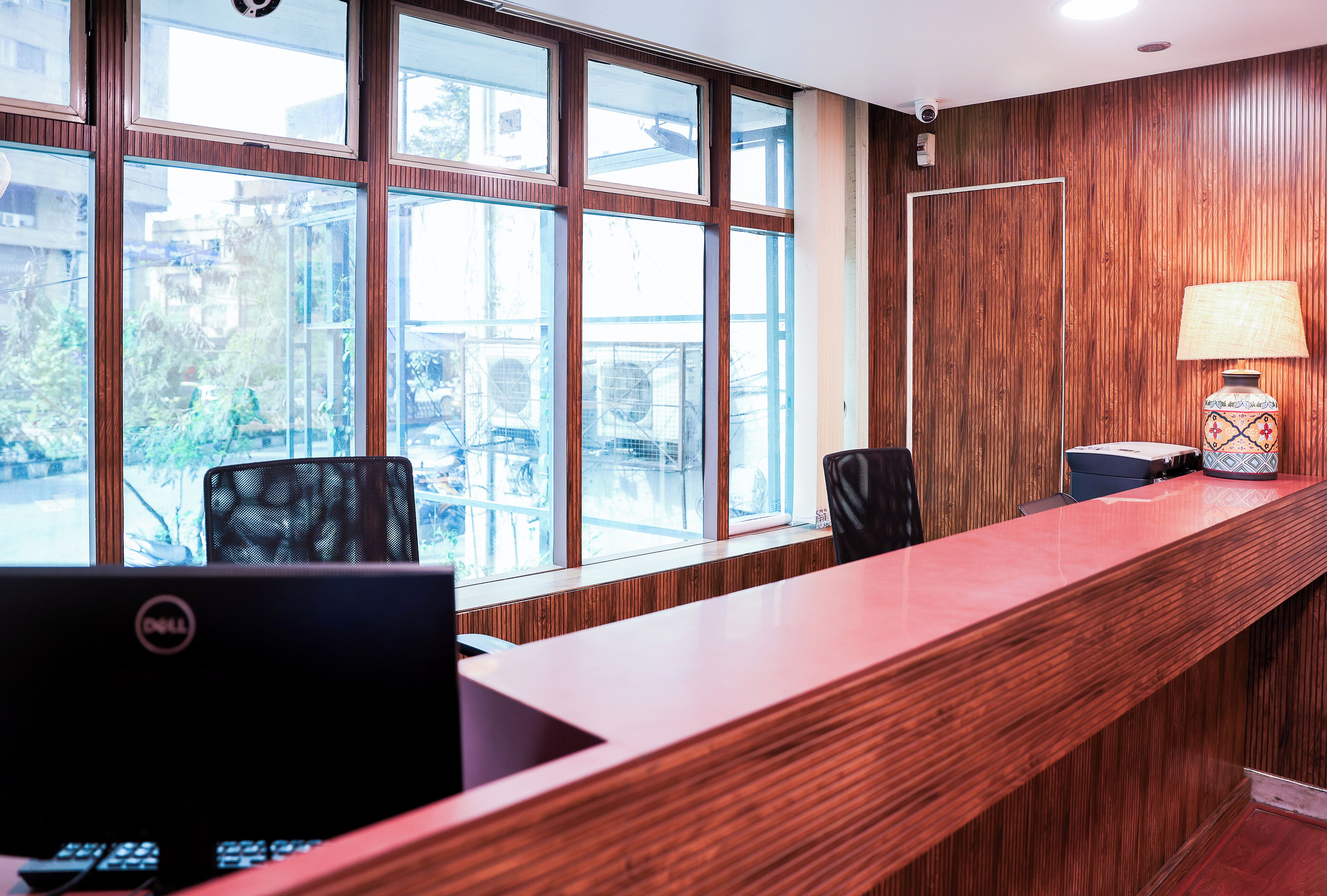 A reception desk with a wooden finish, a computer, and a lamp.