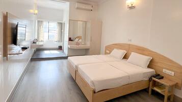 Quarto de hotel com cama de casal, mesa de cabeceira, televisão, espelho, pequena escrivaninha e janela com cortinas.