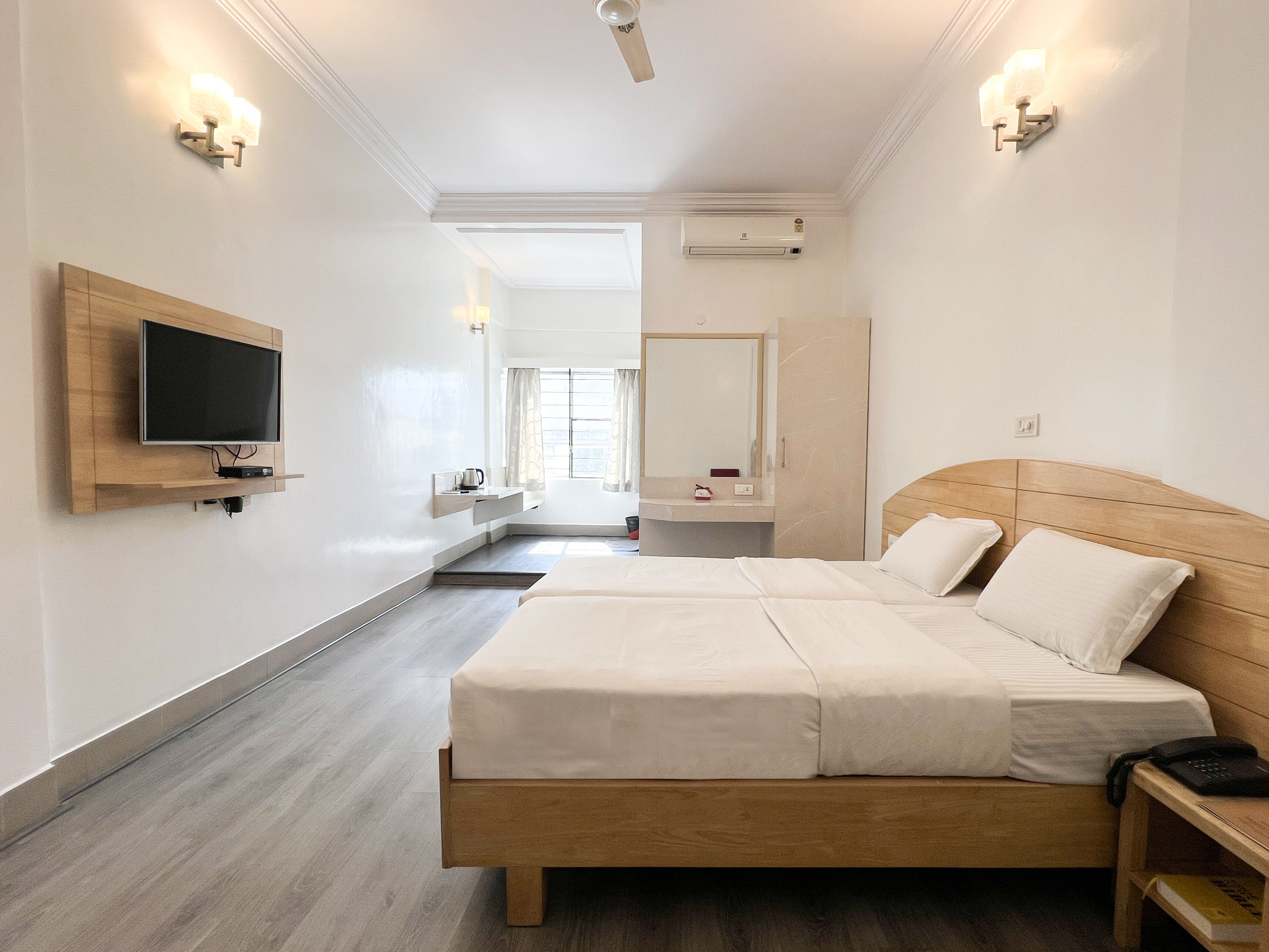 A modern hotel room with a large bed, a TV mounted on the wall, a bedside table, and a mirror.