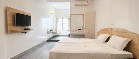 A modern hotel room with a large bed, a TV mounted on the wall, a bedside table, and a mirror.