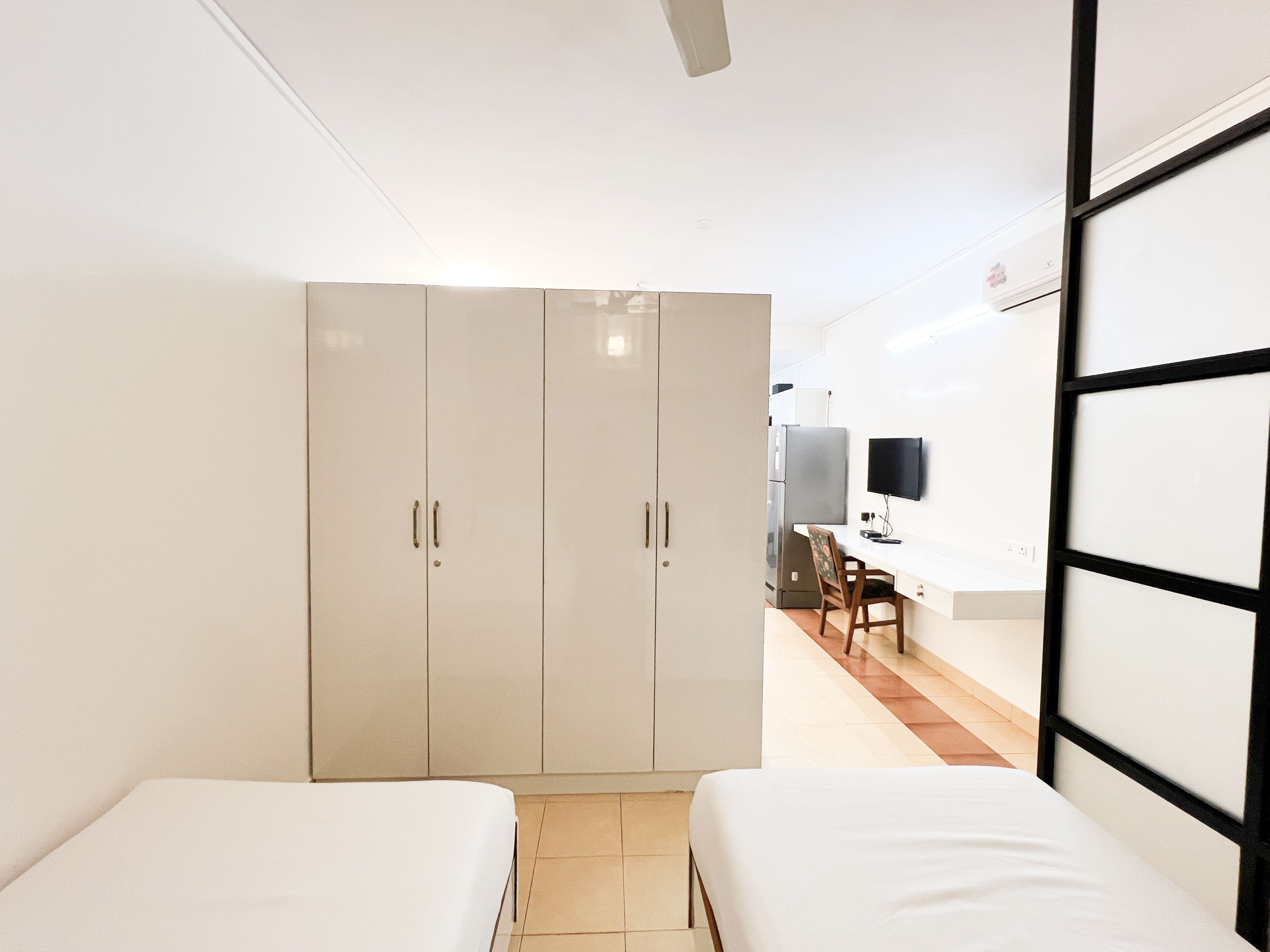 A room with two single beds, a wardrobe, a desk with a chair, and a television on the wall.