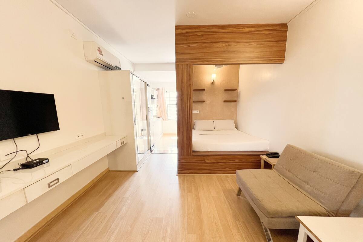Une chambre d’hôtel compacte comprenant un lit, un canapé, un téléviseur fixé au mur et un mur décoratif en bois.
