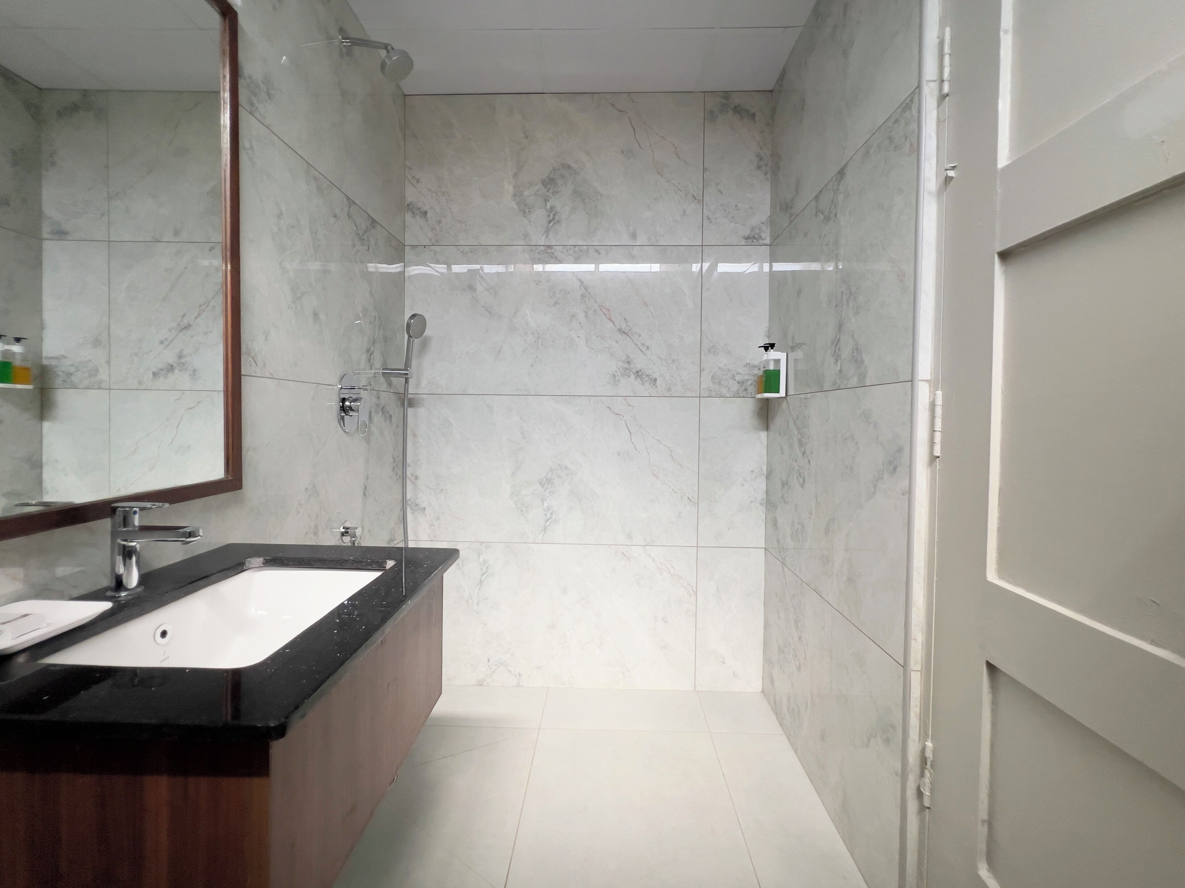 A modern bathroom with a marble shower, a sink with a wooden vanity, and a large mirror.