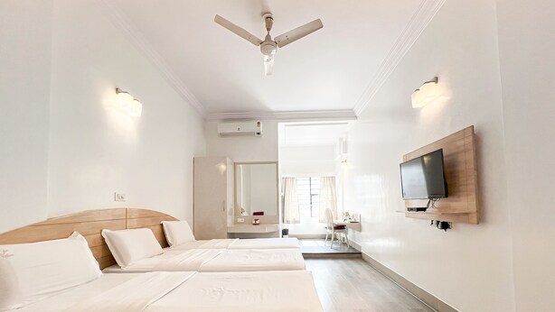 A hotel room with two beds, a TV mounted on the wall, a ceiling fan, and a bathroom visible through an open door. - Hotel Vellara (Bengaluru)