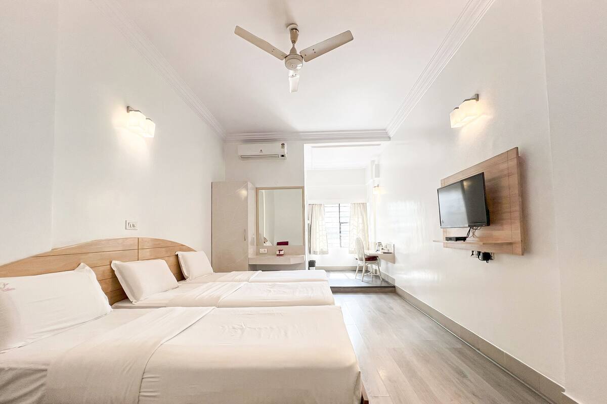 Une chambre d’hôtel avec deux lits, un téléviseur fixé au mur, un ventilateur de plafond et une salle de bain visible à travers une porte ouverte.