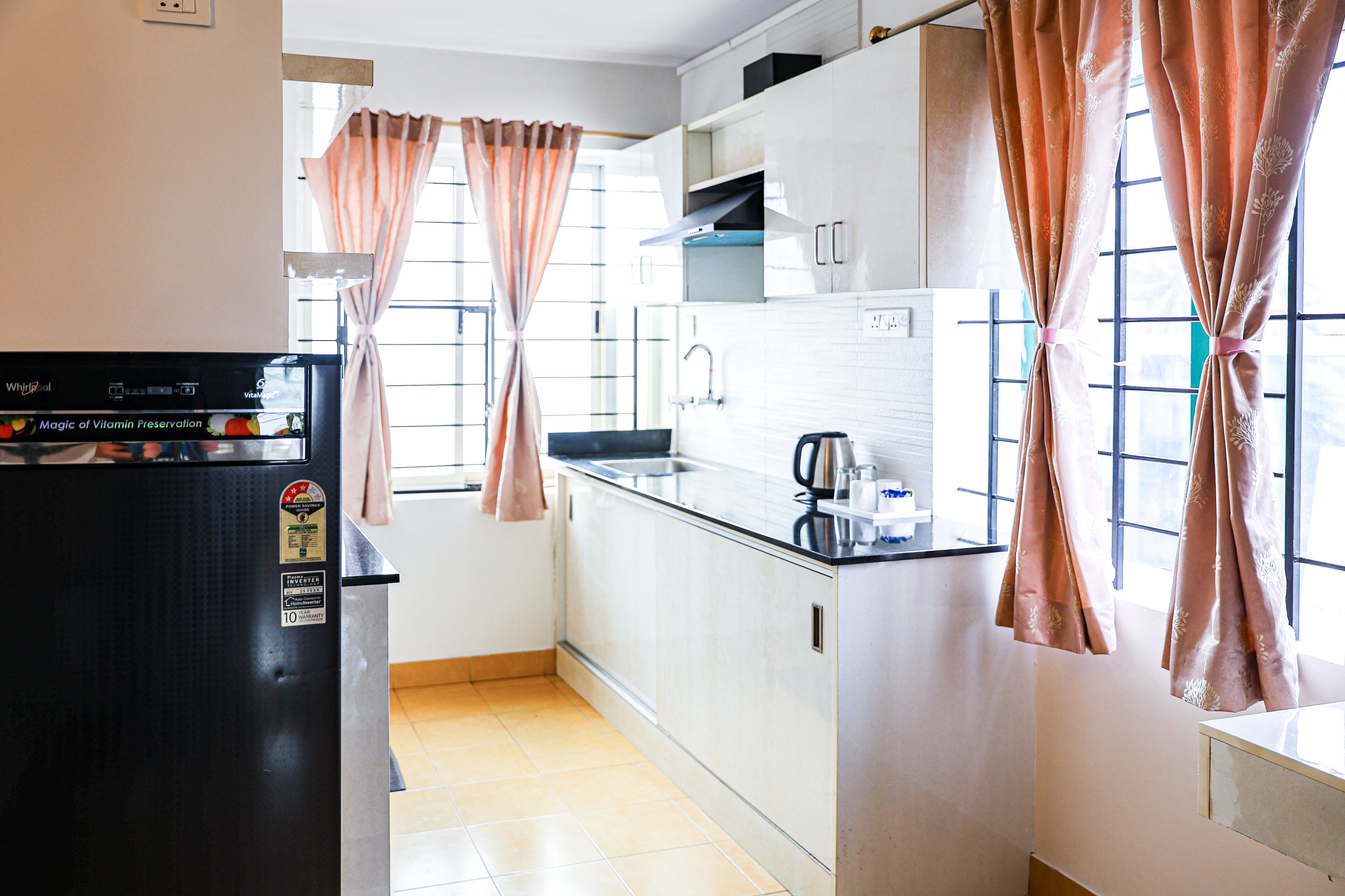 Eine Küche mit Kühlschrank, Spüle und einem Fenster mit Vorhängen.