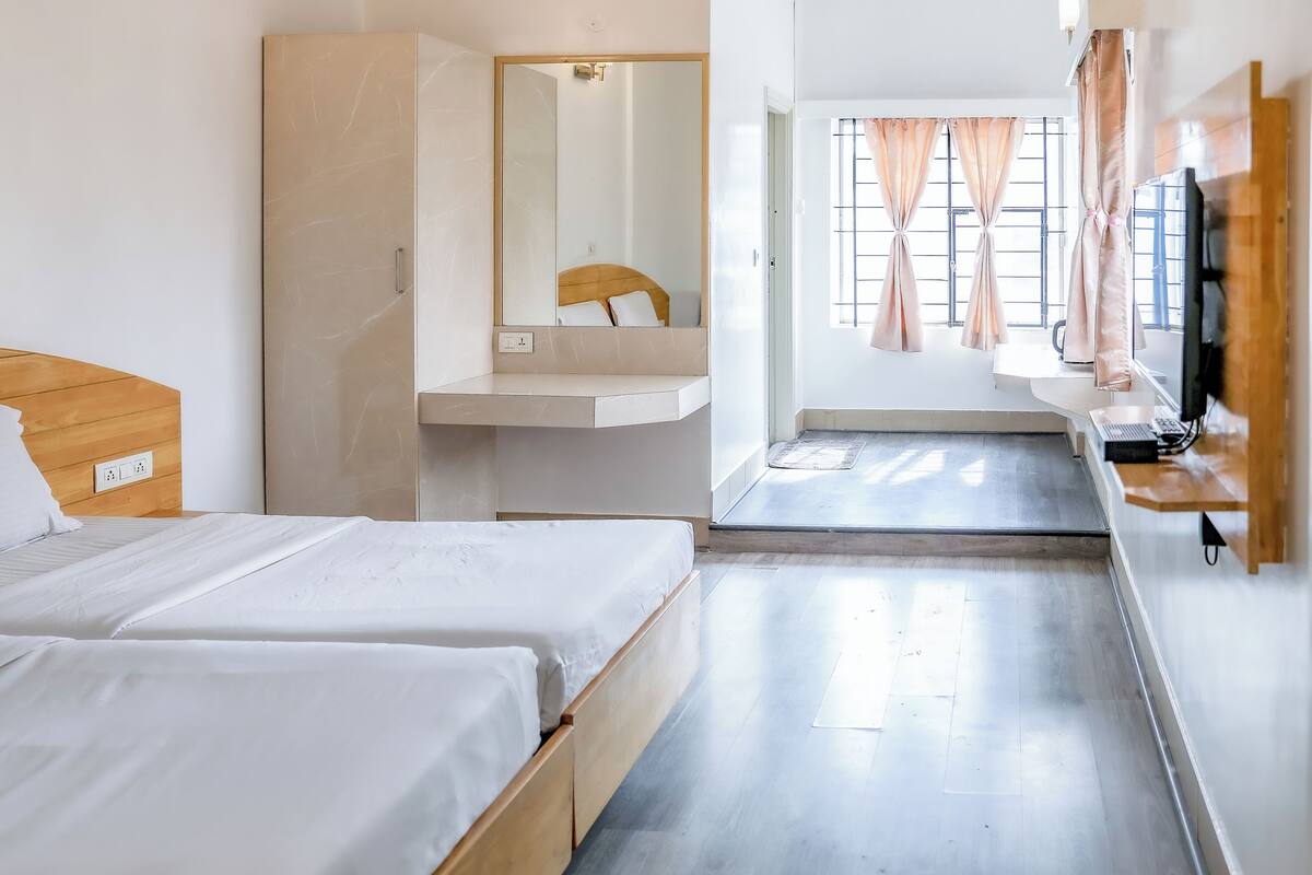 Une chambre d’hôtel avec deux lits, une salle de bain équipée d’un miroir, d’un lavabo et d’une télévision.