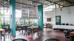 An indoor dining area with tables and chairs, a kitchen area with a counter and sink, and a view of the outside through large windows. - Hotel Vellara (Bengaluru)