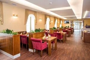 Un vestíbulo de hotel con suelo de madera, sillones tapizados en rojo y una larga recepción.