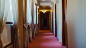 A hotel corridor with a red carpet, wooden doors, and a chandelier.