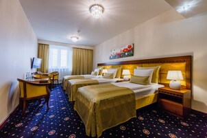 Ein Hotelzimmer mit zwei Betten, einem Schreibtisch mit Stuhl, einem Fernseher und einem Bild an der Wand.
