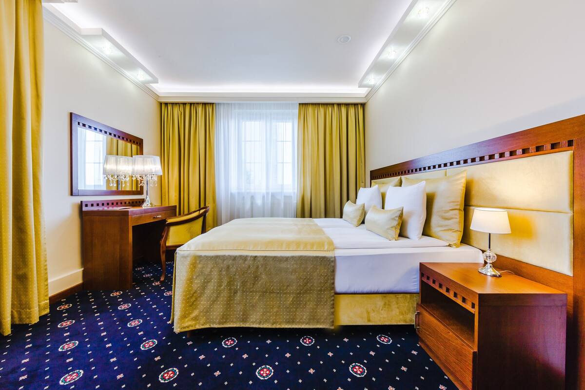 Quarto de hotel com uma cama grande, mesa de cabeceira com abajur, espelho e escrivaninha.