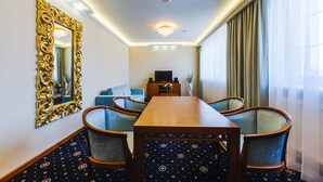 A hotel room with a dining table, chairs, a TV, a sofa, and a large mirror.