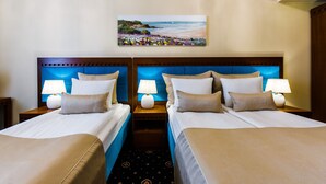 A hotel room with two beds, each with a headboard, bedside lamps, and a painting of a beach scene above the beds.